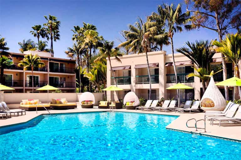 Resort pool with turquoise water surrounded by palm trees, lounge chairs, and colorful umbrellas
