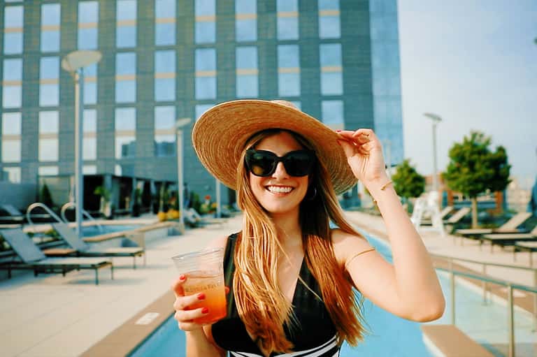 Woman wearing straw hat and sunglasses holding drink by hotel pool