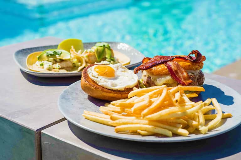 Egg and bacon sandwich with crispy fries served poolside by turquoise water