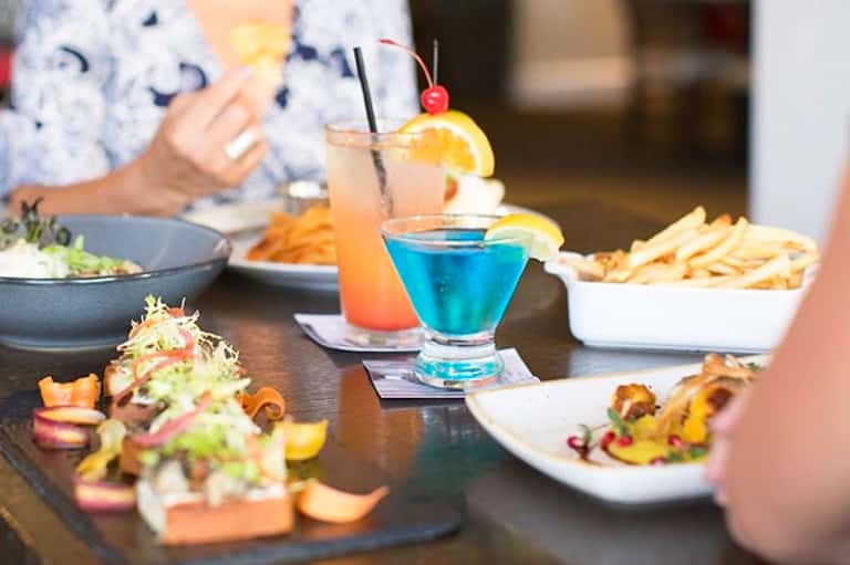 Colorful cocktails and appetizers on a restaurant table with diners in background