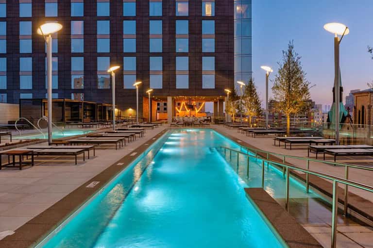Modern rooftop lap pool at dusk with lounge chairs, tall buildings, and city lights