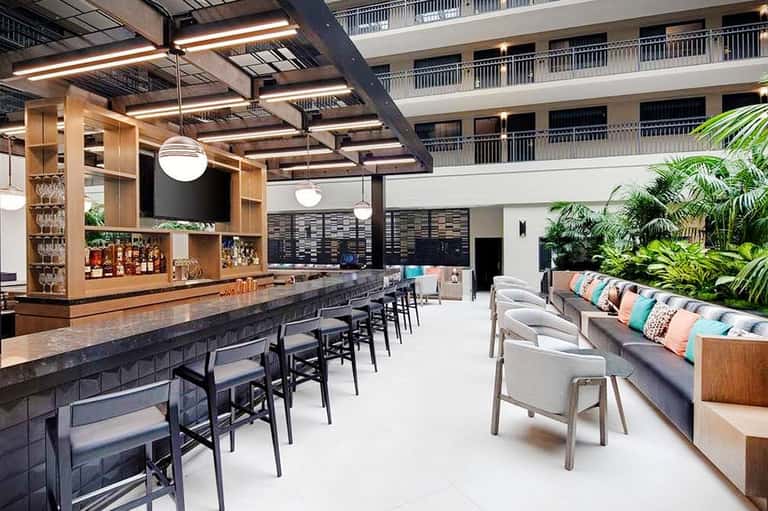 Modern hotel bar and lounge with wooden shelving, colorful cushioned seating, and indoor plants