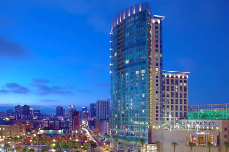 Urban hotel tower illuminated at dusk with city skyline and palm trees visible