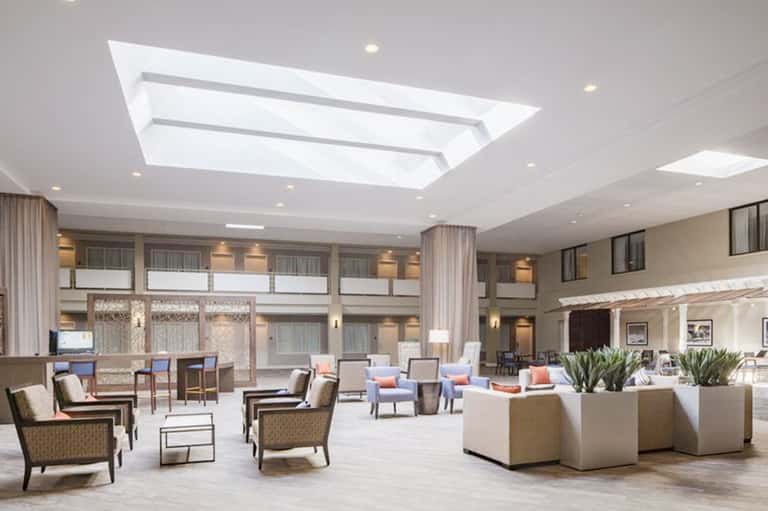 Spacious modern hotel lobby with skylight, seating areas, neutral tones, and contemporary furniture