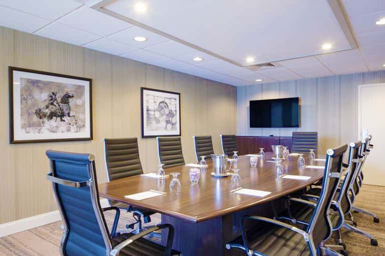 Modern conference room with wooden table, blue chairs, framed artwork, and wall-mounted TV