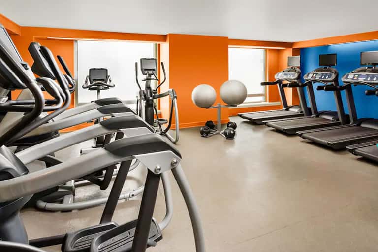 Modern fitness center with elliptical machines, treadmills, and orange accent walls