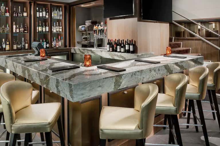 Upscale bar lounge with marble counter, cream leather seating, wine display, and modern decor