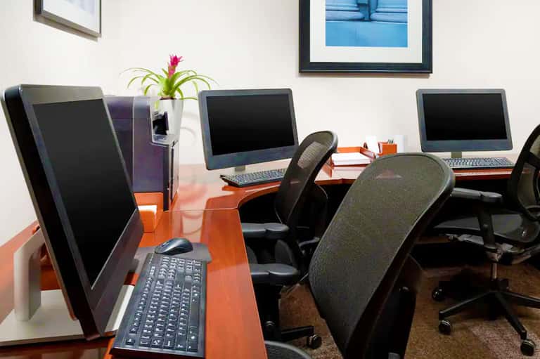 Modern office workspace with orange desks, computer monitors, black chairs, and potted plant