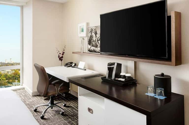 Modern hotel business center with desk, large wall-mounted TV, and city skyline view
