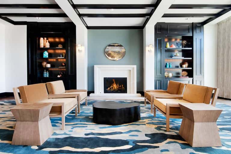 Elegant lounge with fireplace, tan leather seating, blue patterned rug, and built-in shelving