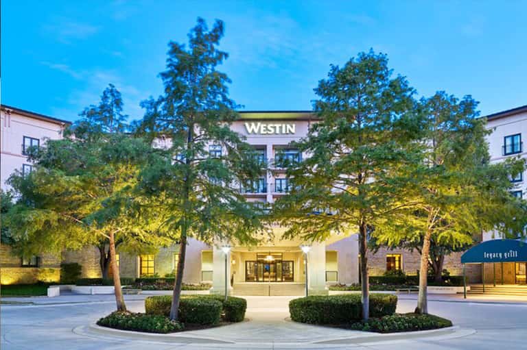 Westin hotel exterior at dusk with illuminated entrance, landscaped courtyard, and manicured trees