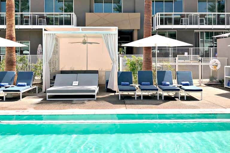 Resort pool area with turquoise water, white loungers, cabana with curtains, and modern building backdrop