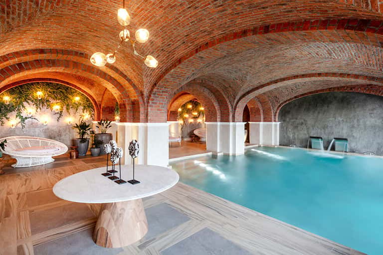 Indoor spa pool beneath ornate brick arches with warm lighting and marble flooring