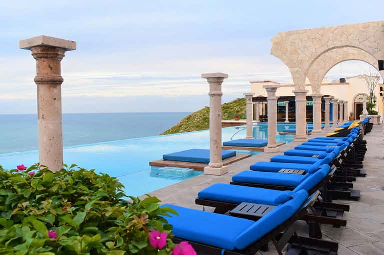 Cliffside infinity pool with blue loungers, Mediterranean columns, and ocean views