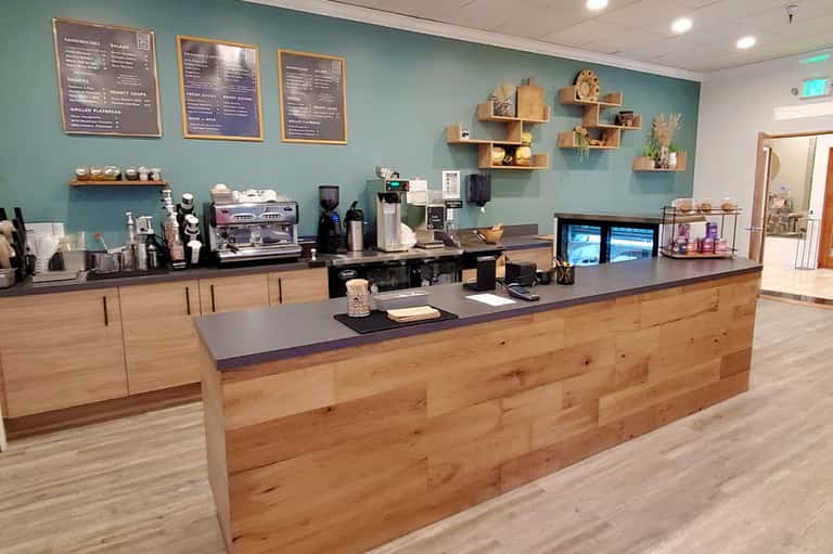 Bright cafe counter with teal walls, wooden cabinetry, menu boards, and espresso machine setup