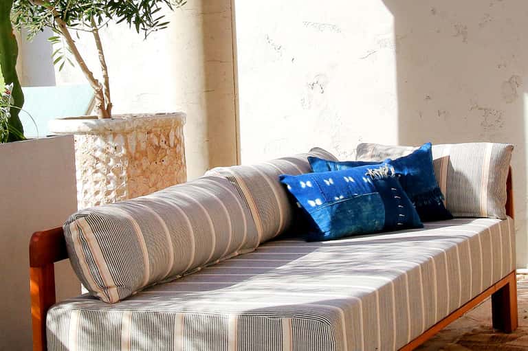 Striped outdoor daybed with blue pillows on a sunlit terrace with potted plant