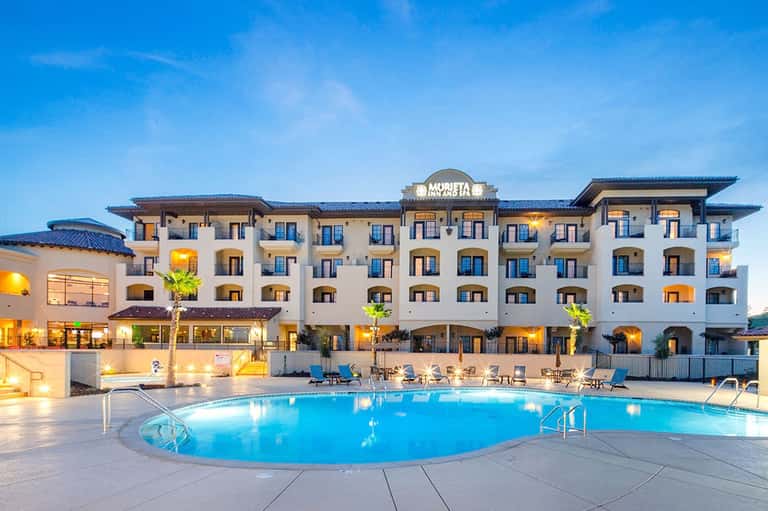 Resort hotel with illuminated pool at dusk, white building facade, blue lighting