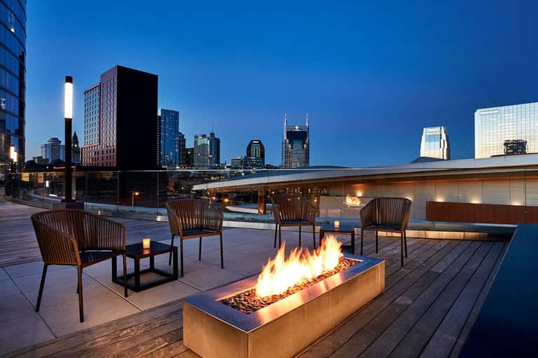 Rooftop terrace at dusk with fire pit, lounge chairs, and city skyline view