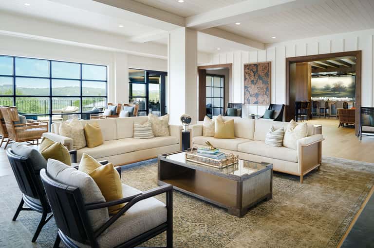 Luxury living room with cream sectional sofas, yellow accent pillows, and expansive windows overlooking countryside landscape