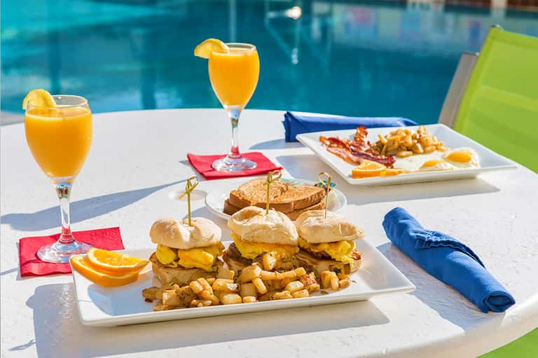 Poolside breakfast spread with burgers, fries, orange juice, and citrus slices