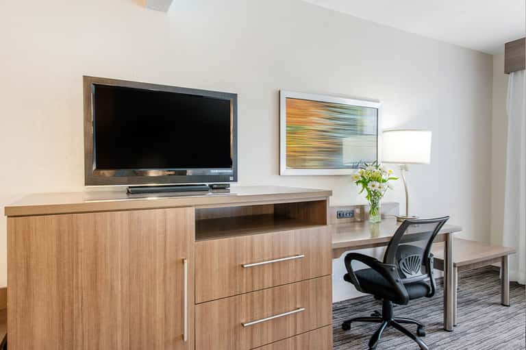 Modern hotel room with wooden entertainment center, TV, desk, office chair, and contemporary decor