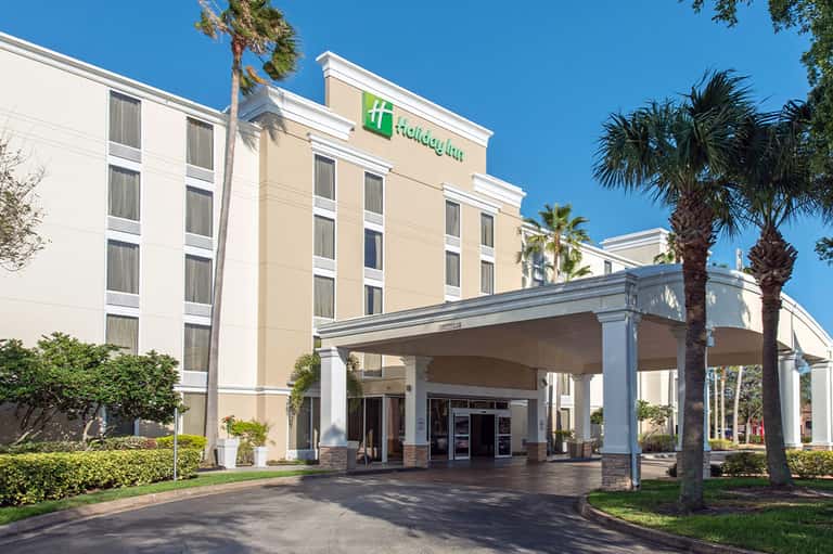 Holiday Inn hotel entrance with covered portico, palm trees, and manicured landscaping