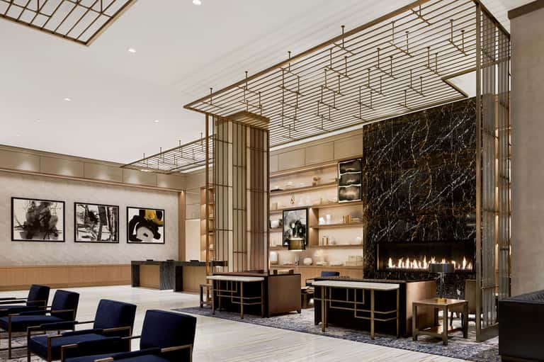 Luxury modern hotel lobby with fireplace, gold metal screens, shelving, and blue seating