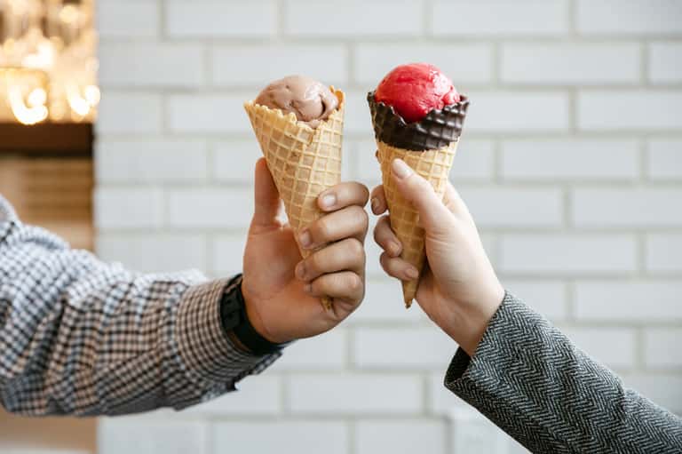 Two ice cream cones held up, one chocolate and one strawberry with chocolate dip