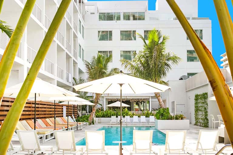 Resort courtyard pool surrounded by white umbrellas, loungers, and palm trees