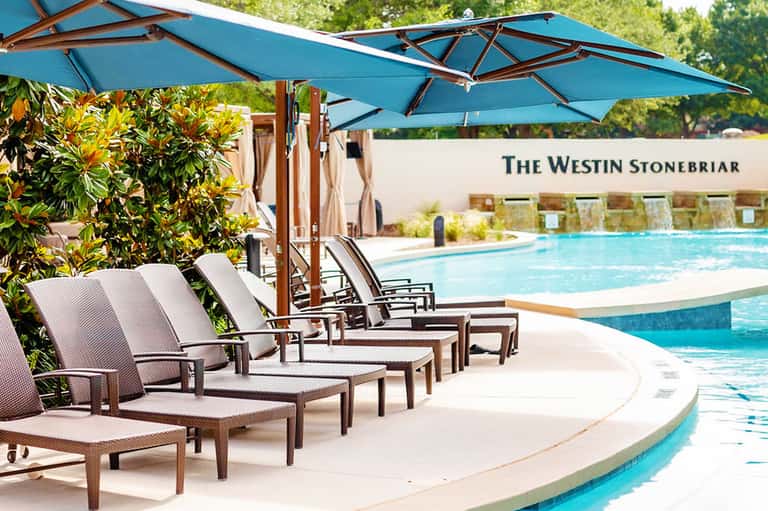 Resort poolside lounge chairs with blue umbrellas and landscaping at The Westin Stonebriar