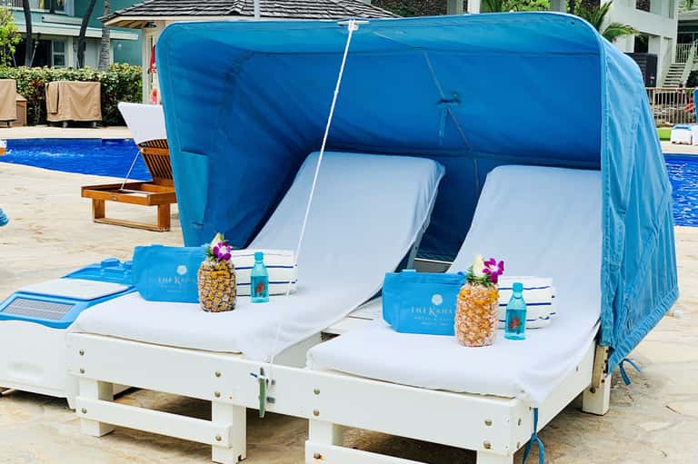 Double cabana lounge bed with blue canopy and pineapple-themed amenities by the pool
