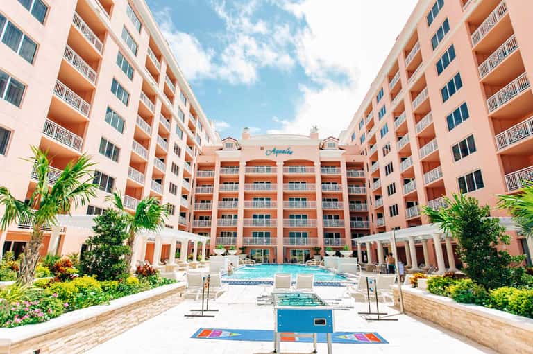 Courtyard pool at Aquila resort surrounded by coral-pink apartment buildings with white railings and palm trees