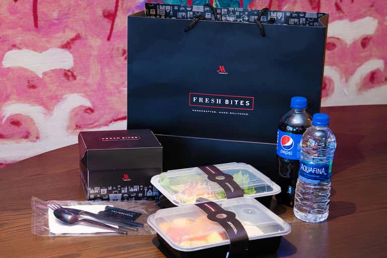 Fresh Bites catering delivery with prepared meals, beverages, utensils, and branded shopping bag on wooden table