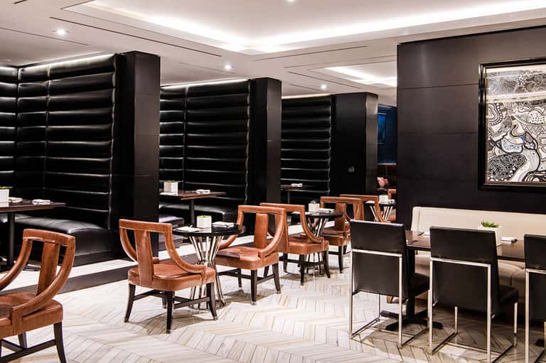 Modern hotel lounge with black padded walls, wooden chairs, and geometric floor pattern