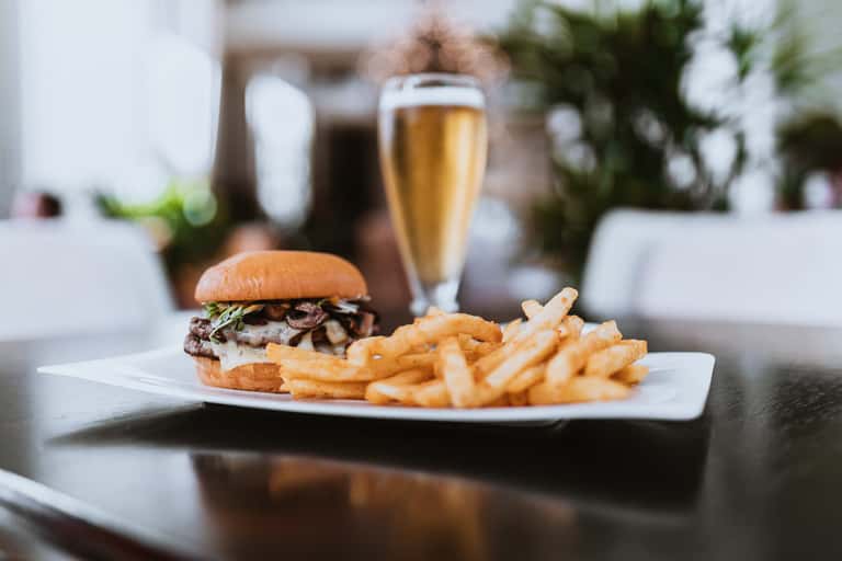 Gourmet burger and fries served with champagne on white plate overlooking resort