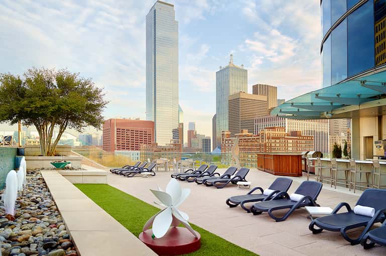 Modern rooftop lounge with dark blue chaise lounges overlooking a city skyline with tall buildings