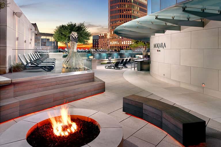 Rooftop lounge at dusk with fire pit, lounge chairs, and city skyline views