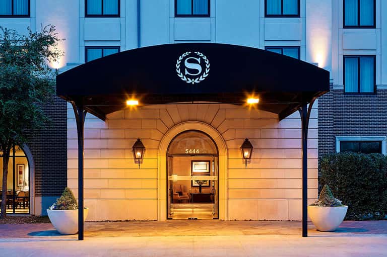 Elegant hotel entrance at dusk with black awning, illuminated doors, brick facade, potted plants, modern architecture
