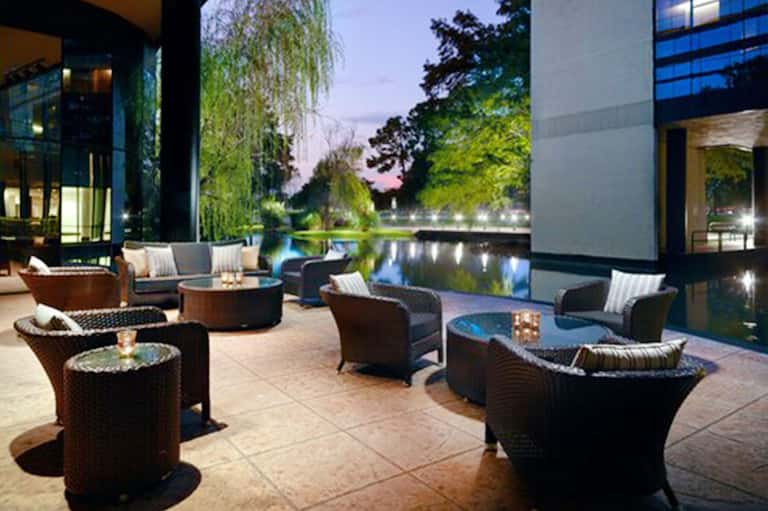 Modern outdoor patio with dark wicker seating, fire pits, and illuminated waterway at dusk