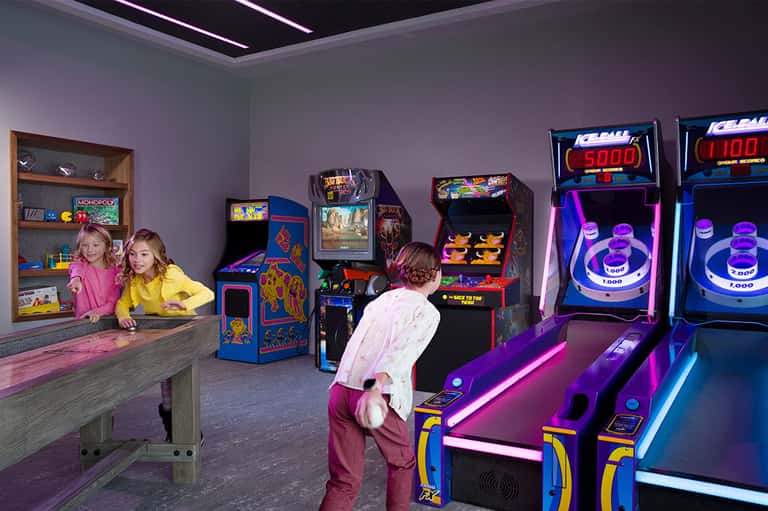 Children playing arcade and vintage games in neon-lit game room with Monopoly display