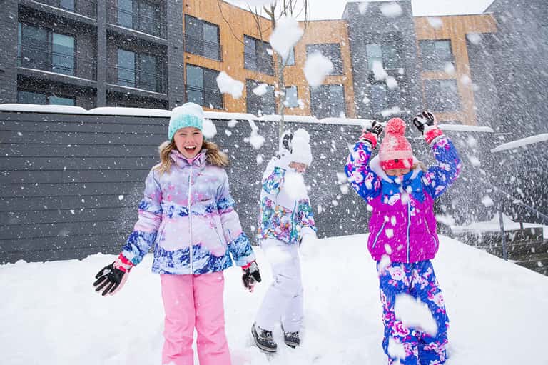 Children playing in snow wearing colorful winter coats and hats in urban courtyard