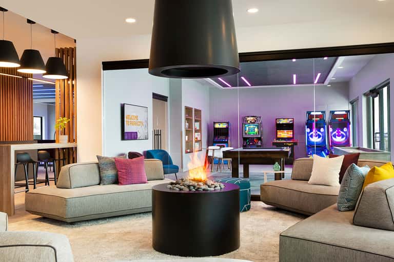 Contemporary lobby lounge with fireplace, arcade games, colorful seating, and purple accent lighting