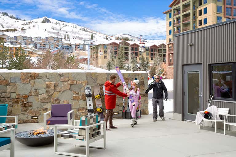 Mountain ski resort terrace with fire pit, modern furniture, snow-covered slopes, and residential buildings
