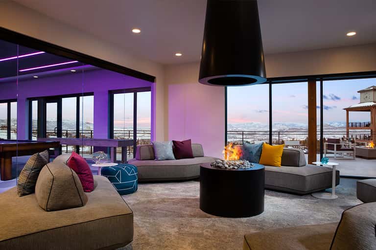 Luxury penthouse lounge with purple accent walls, panoramic city views, fireplace, and contemporary seating