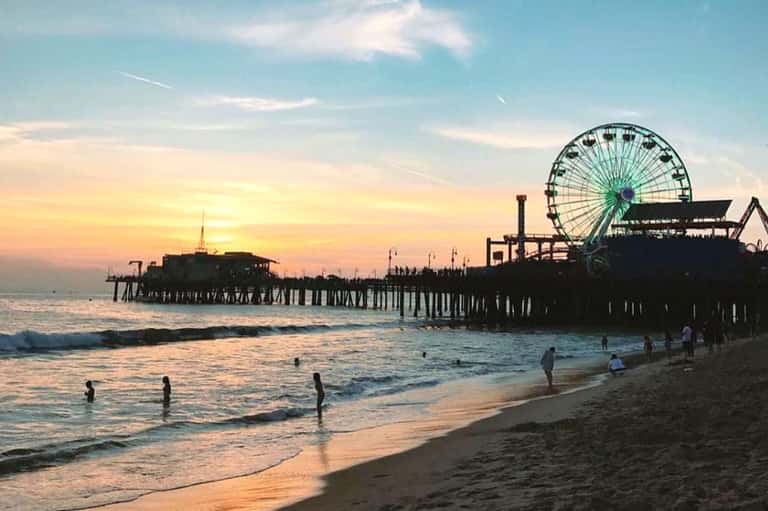 Beach scene at sunset with pier, Ferris wheel, and people swimming in the ocean