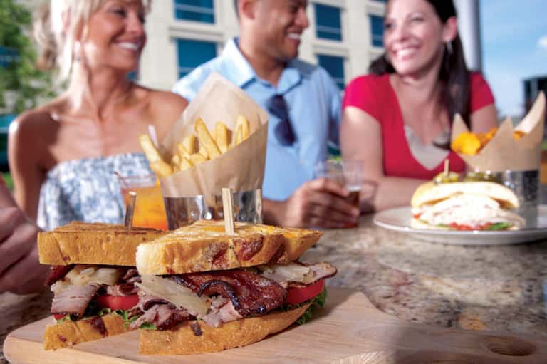 Group dining outdoors with gourmet sandwich and french fries on table