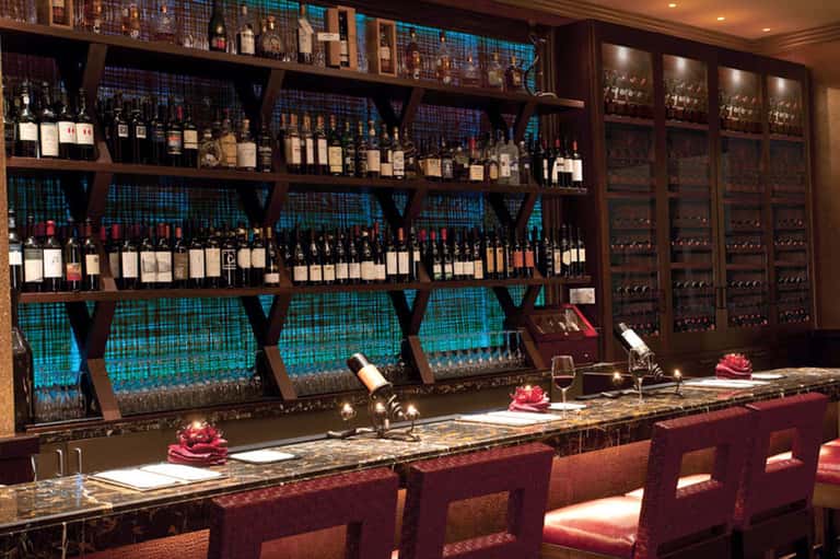 Upscale wine bar with extensive bottle collection on wooden shelves and teal backlighting