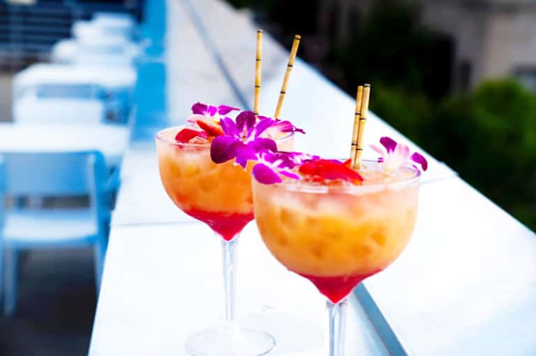 Tropical cocktails with pink syrup base and orchid flower garnish by pool