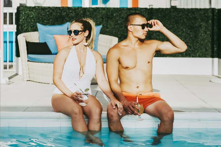 Couple in swimwear sitting poolside wearing sunglasses at a resort