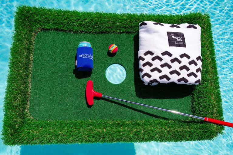 Golf-themed poolside setup with putter, ball, drink cooler, and towel on green turf mat